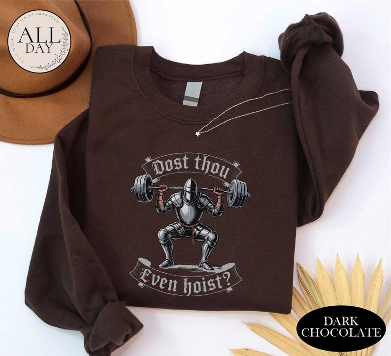 A brown t-shirt with a graphic design depicting a knight lifting a barbell, accompanied by the text "Post thou Even hoist?"