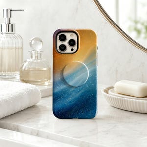 May include: A smartphone case featuring a gradient design that transitions from a warm golden yellow at the top to a deep navy blue at the bottom, accented with a fine white speckled pattern and a matching circular collapsible grip on the back.
