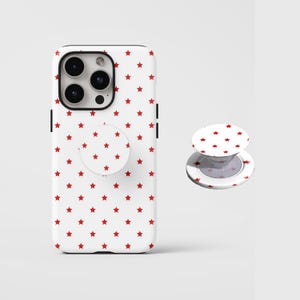 May include: A white phone case and matching phone grip featuring a repeating pattern of small red stars. The phone case is shown with a phone inside, and the grip is shown separately.