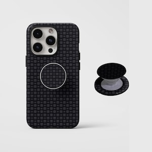 May include: Black phone case and matching PopSocket featuring a repeating pattern of small skulls. The phone case is fitted on a smartphone, and the PopSocket is positioned to the side. The background is plain white.