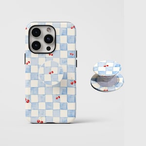 May include: A phone case and matching phone grip featuring a blue and white checkered pattern with red cherry illustrations. The phone case is designed to fit a smartphone, and the grip is a circular pop-out style.
