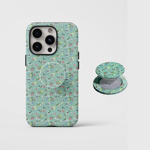 May include: A mint green phone case and matching pop socket featuring a floral pattern with small red, yellow, and blue flowers. The phone case is designed to fit a smartphone, and the pop socket is attached to the back.