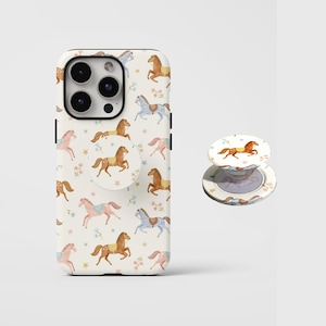 Könnte beinhalten: Eine weiße Handyhülle und ein passender Pop-Socket mit einem sich wiederholenden Muster aus Aquarellpferden in Braun-, Rosa- und Blautönen mit floralen und sternförmigen Akzenten. Die Handyhülle hat ein schwarzes Kameramodul.