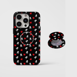 May include: A black smartphone case and a matching circular phone grip, both featuring a repeating pattern of small white skulls with crossbones and solid red hearts scattered across the surface against a solid black background.