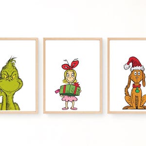 Puede incluir: Tres láminas de pared enmarcadas con personajes de dibujos animados. La lámina de la izquierda muestra una criatura verde con una sonrisa. La central muestra un personaje rubio con vestido rosa sosteniendo un regalo verde. La derecha muestra un perro marrón con un gorro rojo.