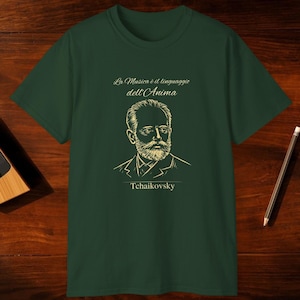 May include: Dark green t-shirt featuring a portrait of Tchaikovsky with the Italian text "La Musica è il linguaggio dell'Anima". A wooden metronome and pencil are on a wooden surface.