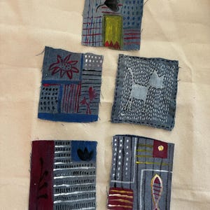 May include: Five small, square fabric patches with hand-painted designs. Each patch features a unique combination of colors and patterns, including floral motifs, geometric shapes, and abstract elements. The patches are arranged on a neutral background.