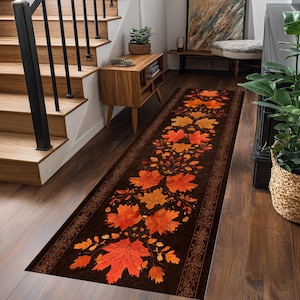 Puede incluir: Una alfombra larga y rectangular con un fondo marrón oscuro y un patrón repetido de hojas de otoño naranjas y amarillas. La alfombra tiene un borde decorativo y está colocada sobre un suelo de madera.