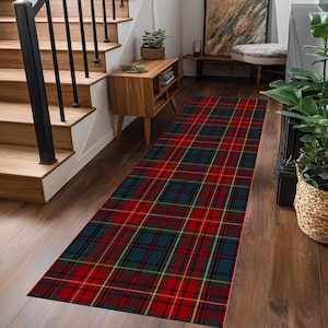 Puede incluir: Una alfombra rectangular con un diseño a cuadros rojo, azul marino, amarillo y negro. La alfombra está colocada sobre un suelo de madera en un pasillo, cerca de una escalera de madera y un pequeño mueble de madera.