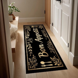 Puede incluir: Alfombra de cocina rectangular negra con borde floral y de hojas doradas. La alfombra presenta las palabras "Bon Appetit" en escritura dorada, junto con un diseño dorado de tenedor y cuchara. La alfombra está colocada en un pasillo.