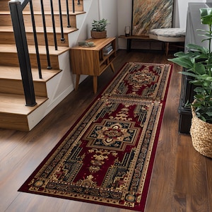 Op de afbeelding: Een lange, rechthoekige loper met een gedetailleerd, sierlijk patroon. Het tapijt heeft een dieprode achtergrond met een centraal medaillonontwerp in marineblauw, goud en zwart. Het tapijt ligt op een houten vloer.