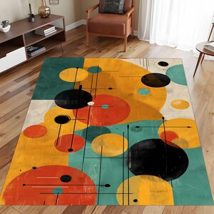 May include: A rectangular area rug with a mid-century modern design. The rug features a pattern of overlapping circles in yellow, orange, black, and teal, with thin black lines. The rug is placed on a hardwood floor.