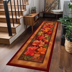 Puede incluir: Una alfombra rectangular con un diseño de hojas de otoño vibrantes. La alfombra presenta hojas grandes y detalladas en tonos rojos, naranjas y amarillos, sobre un fondo dorado cálido y enmarcada por un borde rojo oscuro. Adecuada para pasillos.