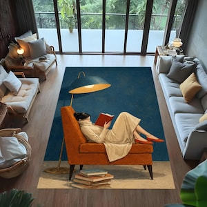 May include: A rectangular area rug featuring a printed illustration of a person in a beige sweater and skirt sitting in an orange armchair, reading a red book under a large blue floor lamp, with a stack of books on the floor beneath the chair.