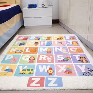 May include: A colorful alphabet rug with a white fluffy border. Each square features a letter and a corresponding illustration, including an apple, a dog, and a zebra. The rug is designed for children.