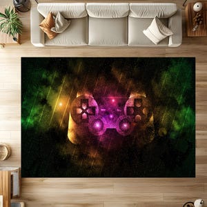 Puede incluir: Una alfombra rectangular con un diseño abstracto y vibrante de un mando de videojuegos. El mando está representado en tonos naranja, morado y amarillo sobre un fondo oscuro con acentos verdes y amarillos. La alfombra está diseñada para una sala de estar.