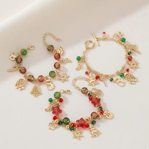 Può includere: Braccialetti con ciondoli natalizi dorati con accenti di perline rosse e verdi. Ogni braccialetto presenta ciondoli festivi come Babbo Natale, fiocchi di neve, alberi di Natale e bastoncini di zucchero. I braccialetti sono esposti su una superficie bianca.