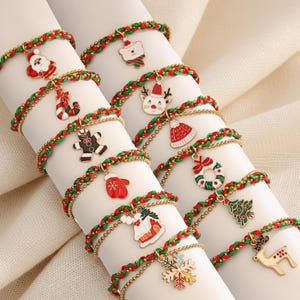 May include: Christmas-themed charm bracelets with red and green braided bands and gold-colored chain accents. Each bracelet features a different holiday charm, including Santa, a reindeer, a gingerbread man, and a snowflake.