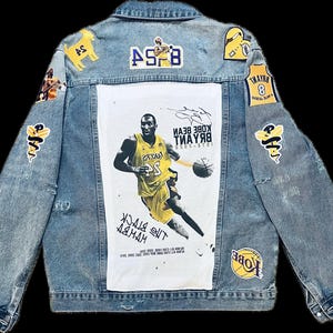 May include: Light blue denim jacket featuring patches and a large white panel with a basketball player graphic. The jacket has multiple patches with yellow and black accents, including the number 8 and the words "The Black Mamba."