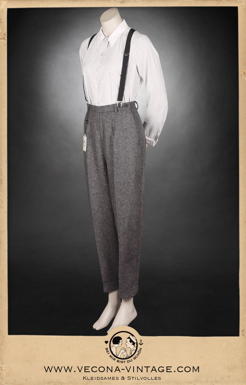 Puede incluir: Pantal&oacute;n de lana gris de cintura alta y pierna ancha. El pantal&oacute;n se sujeta con tirantes negros. El pantal&oacute;n se combina con una camisa blanca abotonada con finas rayas azules. La modelo lleva el atuendo con una expresi&oacute;n neutral.