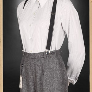 Puede incluir: Una camisa blanca de botones a rayas con tirantes negros y pantalones grises de cintura alta. Los pantalones tienen una peque&ntilde;a etiqueta con un logotipo que dice "Bei mir bist du schon" en alem&aacute;n.
