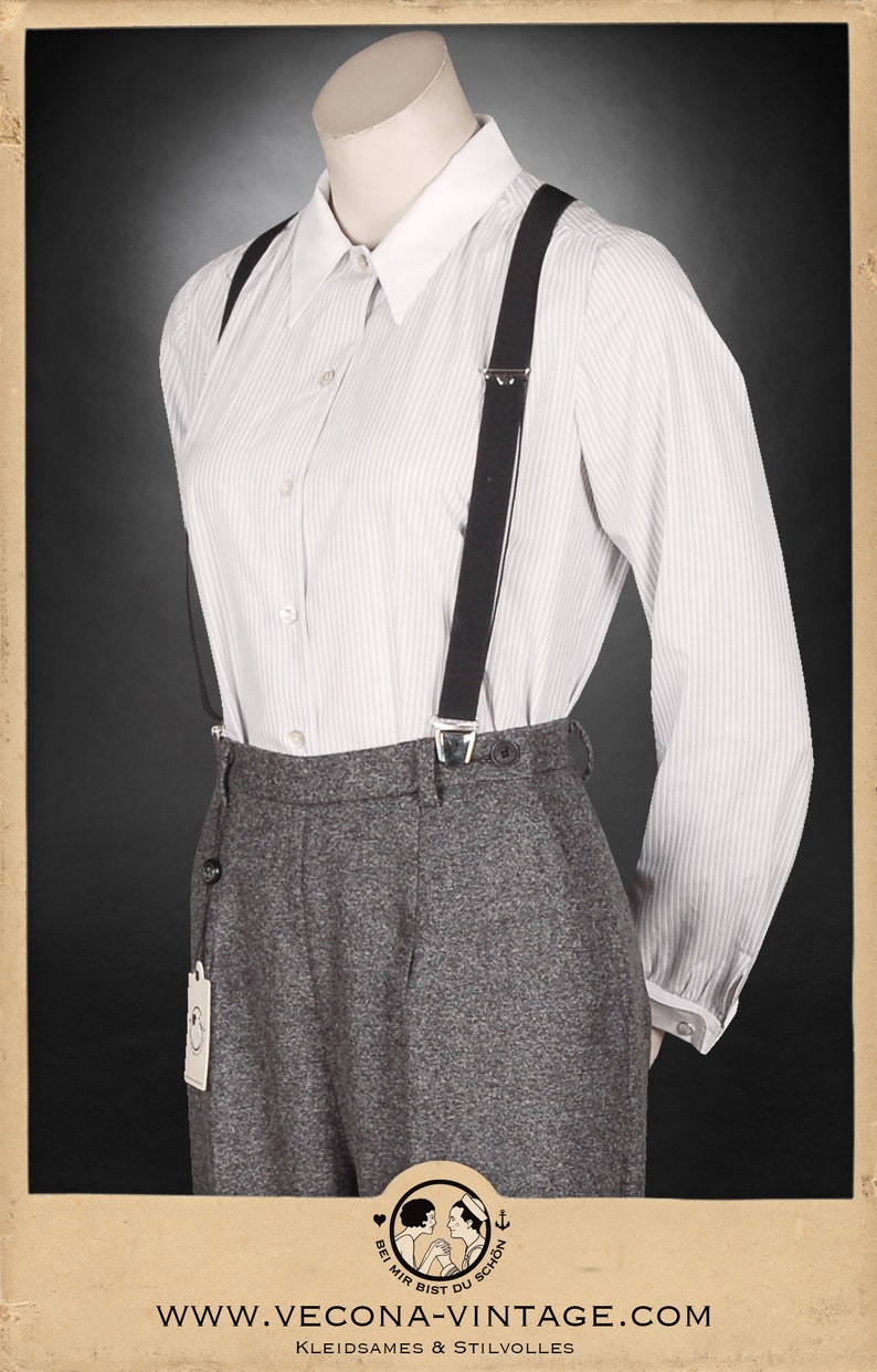 Puede incluir: Una camisa blanca de botones a rayas con tirantes negros y pantalones grises de cintura alta. Los pantalones tienen una peque&ntilde;a etiqueta con un logotipo que dice "Bei mir bist du schon" en alem&aacute;n.