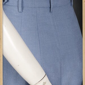 May include: A pair of light blue pants with a white shirt tucked in. The pants have a waistband with belt loops and a zipper fly. The fabric has a subtle texture.