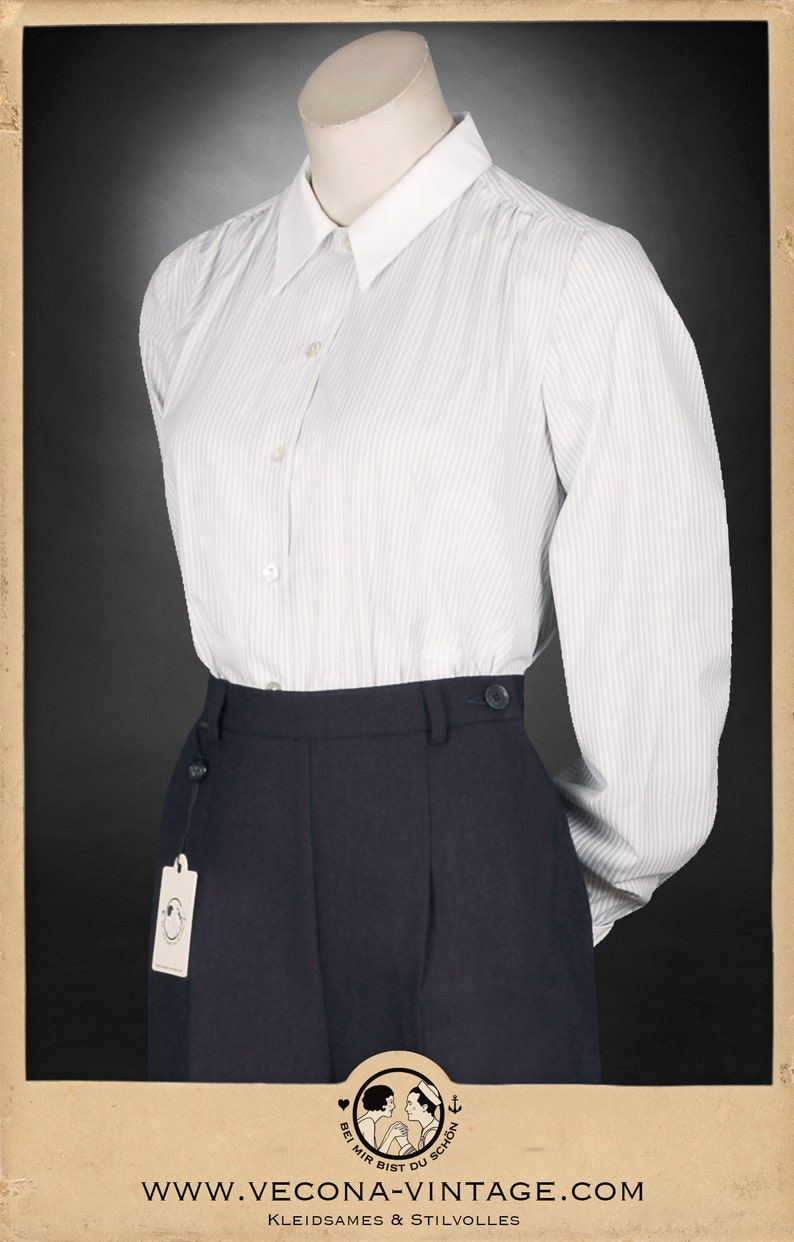 Puede incluir: Una camisa de manga larga a rayas blancas con cuello blanco y una falda azul marino. La camisa tiene un cierre de botones en la parte delantera y la falda tiene una cintura alta y un frente plisado.