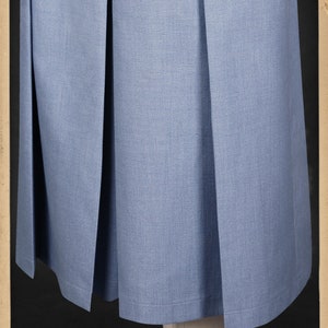 May include: A light blue skirt with pleats. The skirt is made of a smooth fabric and has a simple design. The skirt is hemmed with a thin black line. The image includes the text "www.vecona-vintage.com" and "Kleidsames & Stilvolles".