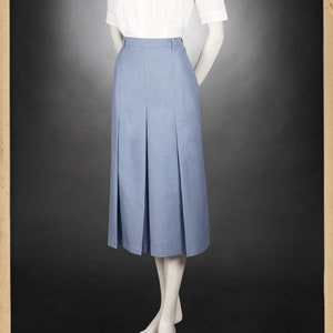 May include: A light blue pleated skirt with a white button-up shirt with a black bow tie. The skirt is knee-length and has a high waist. The shirt has short sleeves and a collar. The model is wearing the outfit on a mannequin.