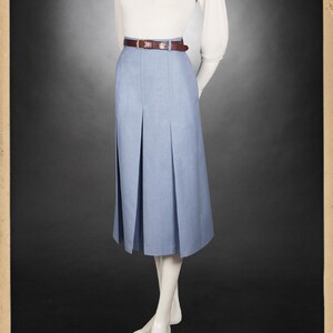 May include: A light blue pleated skirt with a brown belt and a white sweater with a blue patterned scarf. The skirt is knee-length and has a high waist.