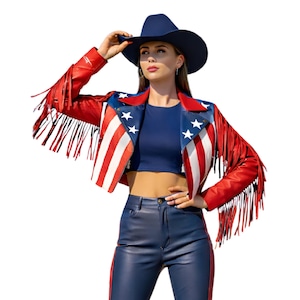 May include: A red, white, and blue leather jacket with fringe, designed with the American flag motif. The jacket features a blue collar with white stars and red and white stripes. The model is wearing a navy blue cowboy hat and matching pants.