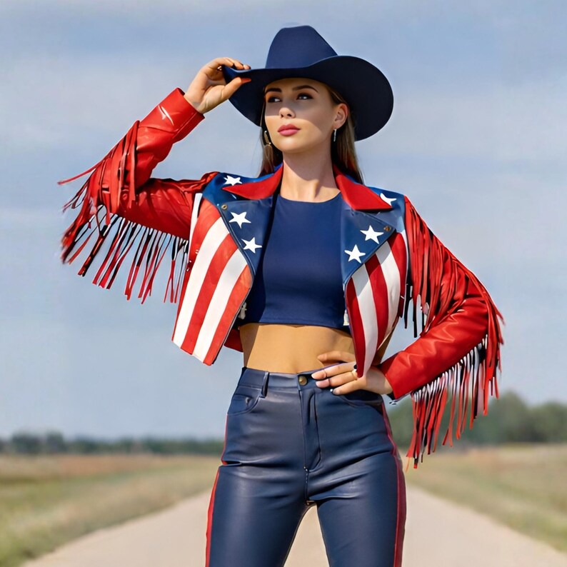 May include: A red, white, and blue leather jacket with fringe, stars, and stripes. The jacket is paired with a navy blue crop top, matching pants, and a navy cowboy hat. The outfit is patriotic and stylish.
