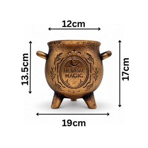 May include: A bronze-colored cauldron with three legs and two side handles, featuring the embossed text HERBAL MAGIC and celestial symbols. Dimensions are 12cm wide at the opening, 19cm wide overall, 13.5cm tall at the body, and 17cm total height.