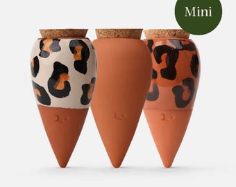 May include: Three terracotta mini planters with cork stoppers. One planter has a white base with black and orange leopard print. The other two are solid terracotta. The word "Mini" is in a green circle in the top right corner.