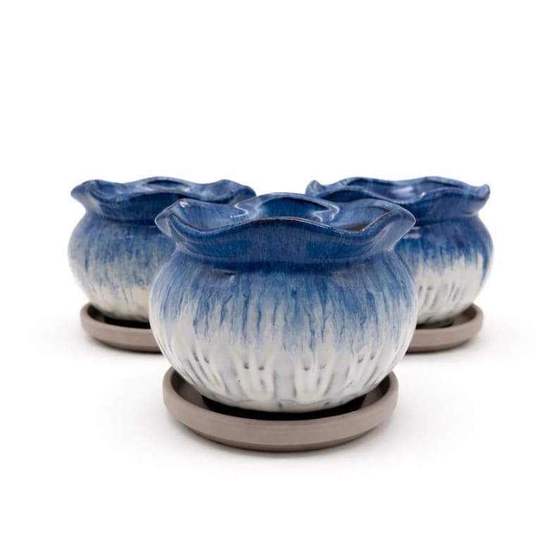May include: Three ceramic flower pots with a blue and white glaze. The pots have a ruffled rim and sit on gray saucers. The pots are approximately 4 inches in diameter and 3 inches tall.