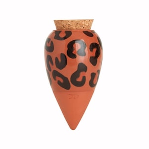 Può includere: Un tappo per bottiglia a forma di goccia, color terracotta, con un tappo in sughero. La bottiglia presenta un motivo leopardato nero. Il tappo è progettato per adattarsi all'apertura di una bottiglia.