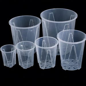 Może przedstawiać: Zestaw przezroczystych plastikowych doniczek do storczyków w różnych rozmiarach. Każda doniczka ma okrągły kształt z otworami drenażowymi na dnie i wewnętrznymi wspornikami pionowymi. Zaprojektowane dla zdrowego wzrostu korzeni.