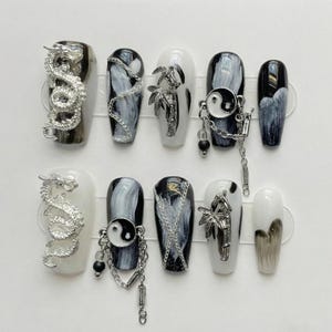 May include: A set of ten artificial nails with various designs. Some nails feature silver dragon, bamboo, or Yin Yang charms. Others have black and white marble or gradient patterns. The nails are in a coffin shape.