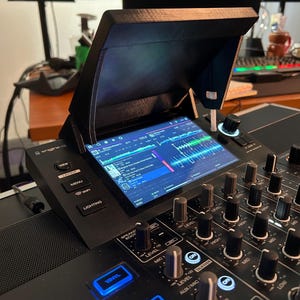 Pode incluir: Um para-sol preto impresso em 3D fixado na tela de um controlador de DJ. O para-sol tem um acabamento fosco e cobre o topo do display, que mostra formas de onda de faixas e a interface do software Engine DJ com vários botões e controles.