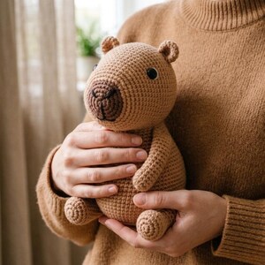Pu&ograve; includere: Un giocattolo di peluche di capibara marrone all'uncinetto con occhi neri e un muso marrone scuro. L'animale di peluche fatto a mano ha piccole orecchie ed &egrave; tenuto davanti a un maglione marrone. Il peluche &egrave; un regalo carino e coccoloso per bambini.