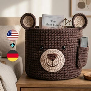 Peut inclure: Un panier en crochet marron en forme d'ours avec un museau et des oreilles beiges. Le panier a une poche sur le côté et est rempli d'un livre, de lunettes et d'un téléphone. Le texte du livre se lit "The Silent Hours".
