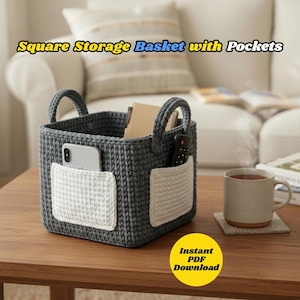 Pode incluir: Um cesto de arrumação quadrado cinzento de croché com dois bolsos brancos e pegas. O texto "Square Storage Basket with Pockets" é visível. O cesto contém um telemóvel, um comando e um caderno. Uma chávena de café está por perto. O texto "Instant PDF Download" também é visível.