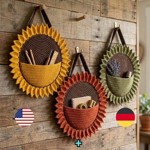 May include: Three circular crochet wall organisers shaped like flowers. The left one is yellow, the centre is orange, and the right is green. Each has a dark brown centre, a hanging strap, and a front pocket containing various small items.