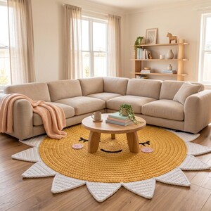Puede incluir: Un sof&aacute; seccional beige con una manta color melocot&oacute;n. Una mesa de centro redonda de madera est&aacute; sobre una alfombra con forma de sol amarilla y blanca. La alfombra tiene un dise&ntilde;o de cara sonriente. Una peque&ntilde;a planta y libros est&aacute;n sobre la mesa.