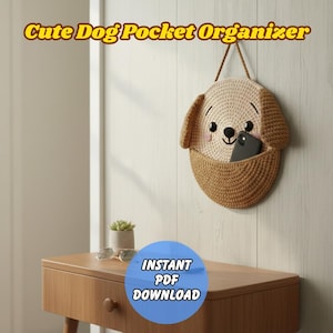 Puede incluir: Un organizador de bolsillo con forma de perro tejido a ganchillo, en beige y marrón, cuelga de una pared. El organizador tiene un bolsillo para guardar cosas y una correa marrón para colgarlo. El texto "Cute Dog Pocket Organizer" está en la parte superior. Hay un teléfono en el bolsillo.