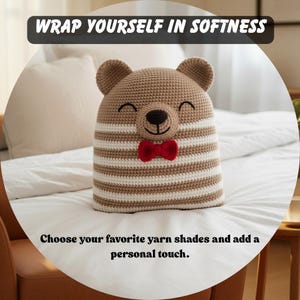 May include: A crocheted bear-shaped pillow with a smiling face and a red bow tie. The bear has brown and white striped body and ears. The text "WRAP YOURSELF IN SOFTNESS" and "Choose your favorite yarn shades and add a personal touch" are displayed.
