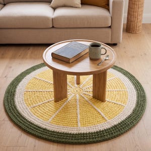 May include: A round, handmade crochet rug with a lemon slice design. The rug features a yellow center with white and green borders. A small wooden table with a book and mug sits on the rug. The rug is approximately 47 inches in diameter.