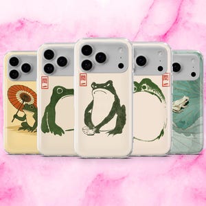 May include: A collection of phone cases featuring Japanese-inspired frog illustrations. Each case showcases a different frog design in shades of green and beige, with a red square symbol. The cases have a clear, protective design.
