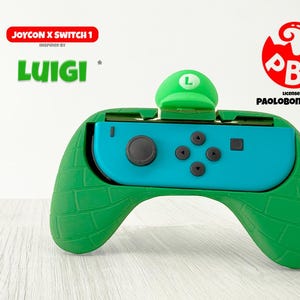 May include: A green and blue Nintendo Switch Joy-Con controller with a green Luigi hat design. The controller has a brick-like texture on the green parts and the word "Luigi" is displayed in green. The controller is inspired by the character Luigi.